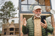 © Miljan Živković - One senior man stand in front of tiny house in day use smart phone
