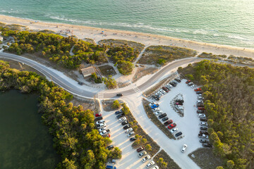 Wall Mural - Parking lot for tourists cars in front of ocean beach with soft white sand in Florida. Popular vacation spot at sunset