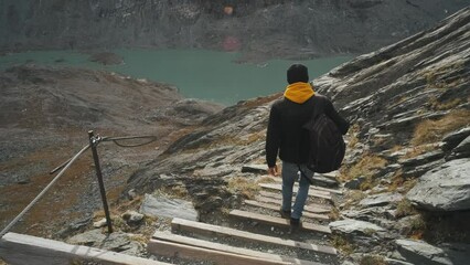 Wall Mural - Young man traveler goes down the path with steps to the glacier enjoys the view of beautiful mountains and glacier along Majestic Grossglockner Mountain Road in Austria