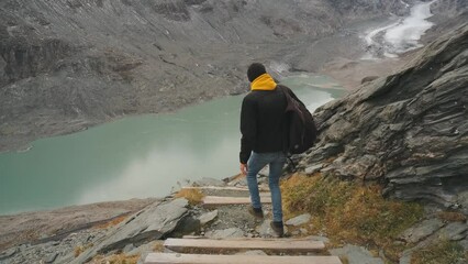 Wall Mural - Young man traveler goes down the path with steps to the glacier enjoys the view of beautiful mountains and glacier along Majestic Grossglockner Mountain Road in Austria