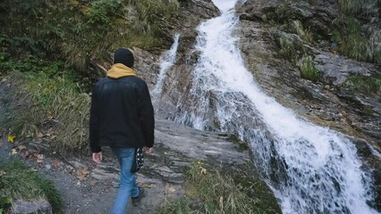 Wall Mural - Man traveler walks Hiking route in the Alps and enjoys the view of a mountain river and waterfall. Incredibly beautiful views in the Alpine mountains.