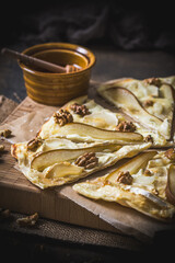 Wall Mural - Pieces of a tarte flambee with pear, goat cheese, honey and walnuts on dark rustic wooden background, vertical