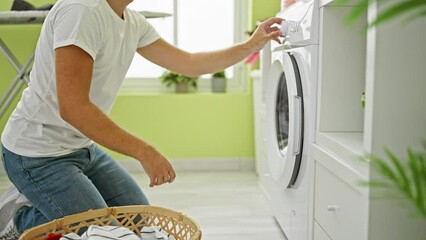 Wall Mural - A young man in a white t-shirt does laundry in a bright green room with a modern washing machine