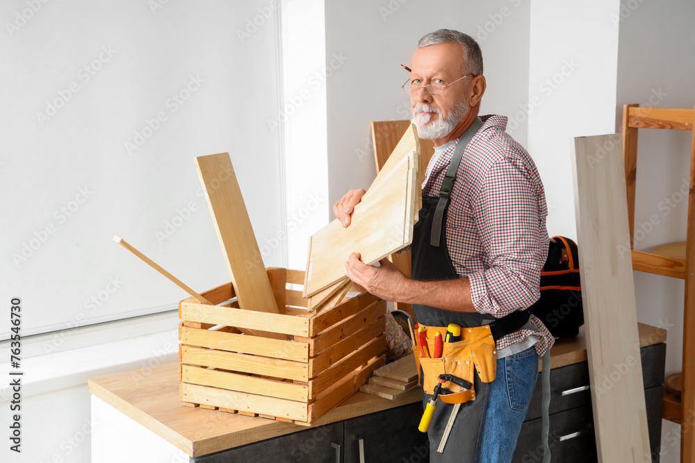 Mature carpenter with wooden planks in workshop