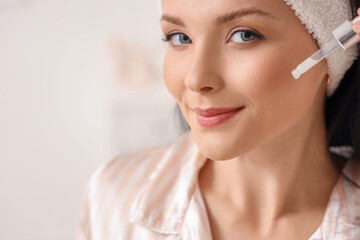 Canvas Print - Beautiful woman applying facial serum in bathroom, closeup