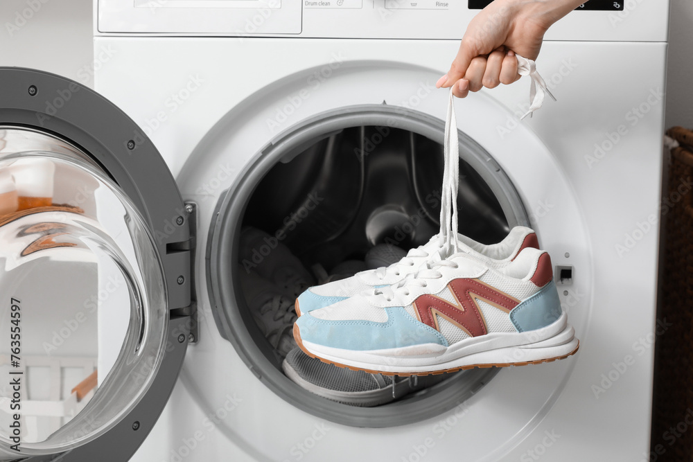 Female hands with sneakers and open washing machine, closeup