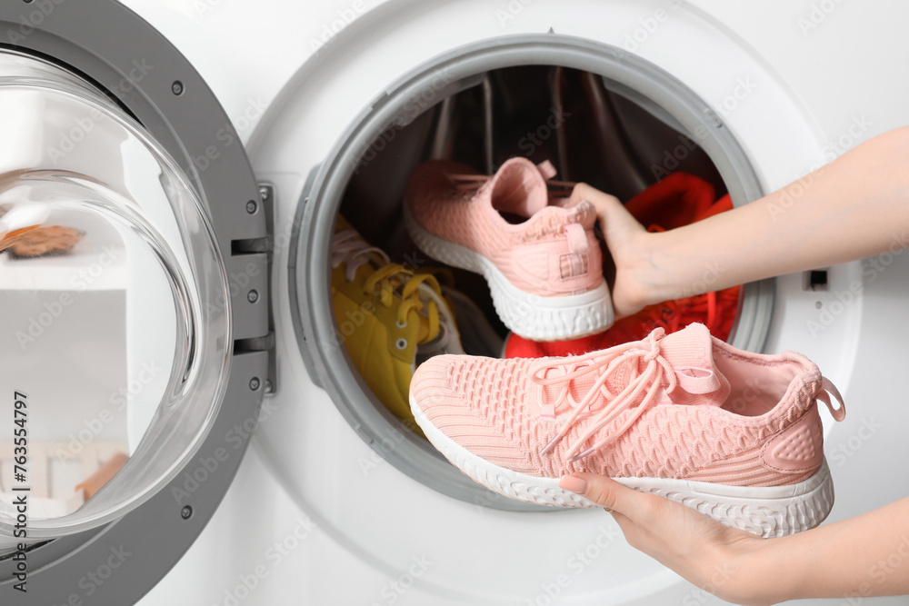 Woman putting sneakers in washing machine, closeup