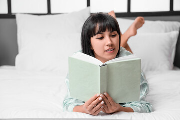 Wall Mural - Young woman reading book on bed at home