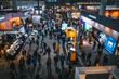 © Ilia Nesolenyi - High-angle view of a bustling tech conference hall filled with people standing around, engaging in discussions and networking during the event