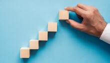 Wooden Cubes In The Form Of A Ladder With A Hand On A Blue Background