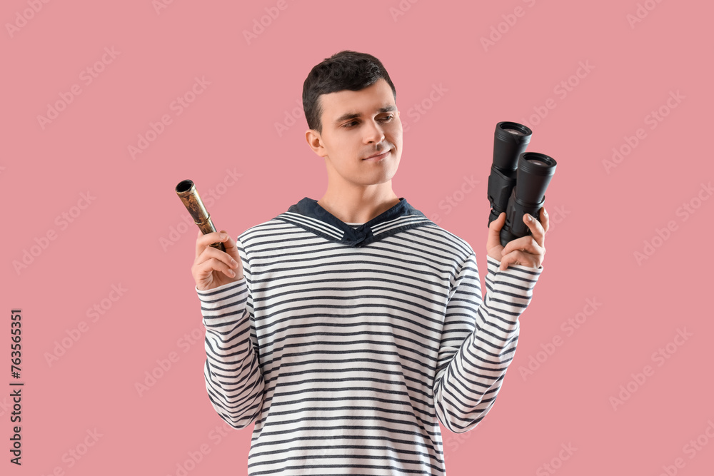 Thoughtful young sailor with spyglass and binoculars on pink background
