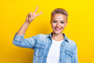 Wall Mural - Photo portrait of pretty young girl show v-sign shopping promo wear trendy jeans outfit isolated on yellow color background