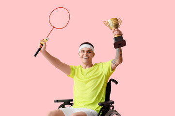 Wall Mural - Male badminton player in wheelchair with racket and gold cup on pink background