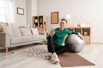 Poster - Sporty young man with fitball using mobile phone at home