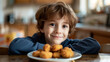 A.young boy at the kitchen table with a plate of tater tots or also known as hush puppies.