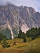 A majestic rocky mountain in the Dolomites rising above a meadow with trees, Italy