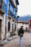 Fototapeta Na drzwi - Young Peruvian man in camo coat, brown sling bag, strolls amidst vibrant, stone rural houses.