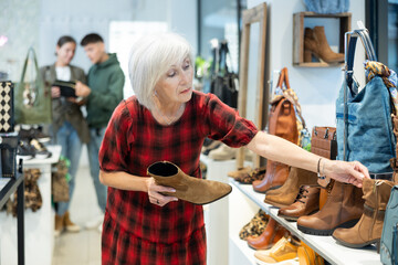 Wall Mural - Elderly woman in casual clothes chooses ankle boots in store..