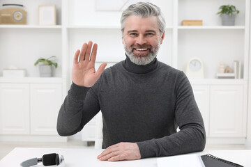 Wall Mural - Man waving hello during video chat at home, view from webcam