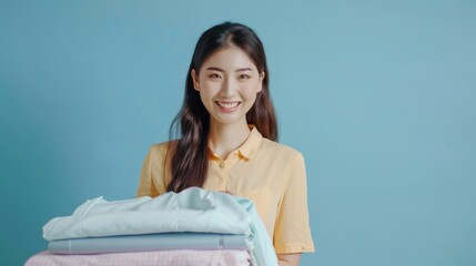 Happy Asian woman with stack of ironed clothes, after using electric steam iron.