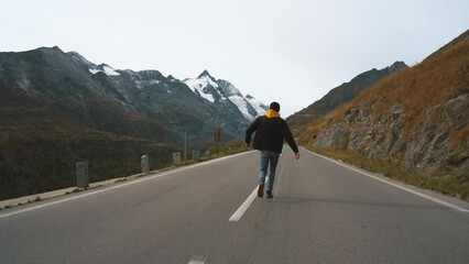 Wall Mural - Man traveler running along a mountain Majestic road Grossglockner Mountain Road in Austria, snow covered sharp peaks of the alpine mountains on background. Incredibly beautiful views in the Alpine
