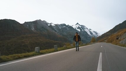 Wall Mural - Man traveler walks along Majestic Grossglockner Mountain Road in Austria, snow covered sharp peaks and glacier of the alpine mountains on background. Incredibly beautiful views in the Alpine mountains
