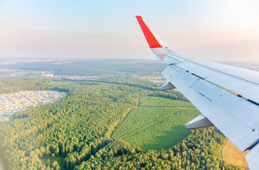 View of airplane wing, blue skies and green land during landing. Airplane window view.