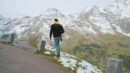 Wall Mural - Man traveler walks along Majestic Grossglockner Mountain Road in Austria, snow covered sharp peaks of the alpine mountains on background. Incredibly beautiful views in the Alpine mountains