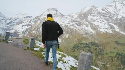 Wall Mural - Man traveler walks along Majestic Grossglockner Mountain Road in Austria, snow covered sharp peaks of the alpine mountains on background. Incredibly beautiful views in the Alpine mountains