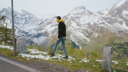 Wall Mural - Man traveler walks along Majestic Grossglockner Mountain Road in Austria, snow covered sharp peaks of the alpine mountains on background. Incredibly beautiful views in the Alpine mountains