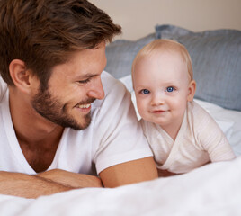 Wall Mural - Happy, sweet and baby with father on bed relaxing, playing and bonding together at home. Smile, love and young dad laying with girl child, infant or kid in bedroom or nursery at family house.