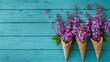 Flowers composition. Fresh lilac flowers in waffle cones on  turquoise wooden  background. Top view.