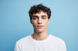 Serene Young Adult Male with Curly Hair Posing in White T-Shirt Against Soft Blue Background, Studio Portrait