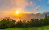 Fototapeta Góry - Embrace the serene sunset from Miradouro do Pico dos Bodes, where the sun rays illuminate São Miguel's verdant landscapes in a soft mist.