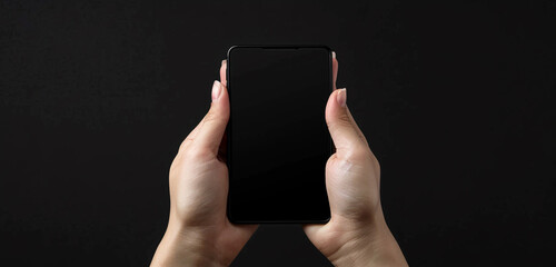 Wall Mural - Detailed front view shot of a person grasping a black screen mobile with both hands, fingers elegantly positioned on the device, against a seamless black background