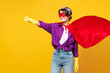 © ViDi Studio - Side view young woman wears purple shirt rubber gloves super hero suit mask casual clothes do housework tidy up clench fist isolated on plain yellow background studio portrait. Housekeeping concept.