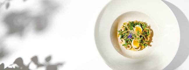 Canvas Print - Healthy salad with squid and avocado on white plate with harsh shadows. Calamari salad with vegetables and eggs on white background with shadows of leaves. Summer food menu.