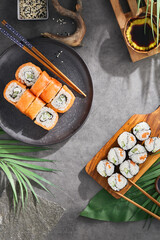 Canvas Print - Japanese food philadelphia maki and salmon sushi roll on ceramic plate on gray stone background. Maki sushi set on concrete background with palm leaves and shadow. Aesthetic composition with sushi.