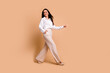 © deagreez - Full length photo of positive dreamy woman wear white shirt carefree walking empty space isolated beige color background
