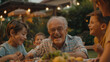 Elderly man and his family having fun at the backyard barbecue. Happy kids with grandpa enjoying food together in their garden during summer vacation