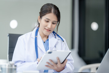 Wall Mural - Portrait of mix race asian middle age female doctor in white lab coat and stethoscope while consult online in laptop. advice on good mental health management and medical treatment costs.