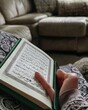 a Muslim reading Holy Quran with open pages in Ramazan during sunshine in a modern house while sitting on a sofa in the morning