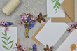 Little flowers, white paper, envelopes on a table. White sheet of paper to fill in the content, flat lay. 