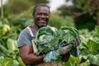 A smiling black working man carrying cabbages in his hands while wearing work gloves in the farm with green big bushes and trees and clear white sky in the background