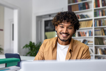 Wall Mural - A happy young male professional is engaged in his work on a laptop, smiling in a bright office setting.