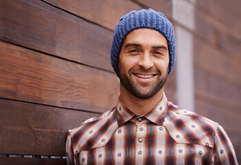 Poster - Portrait, smile and man on wood wall background outdoor in casual clothes, outfit or apparel. Face, happy and stylish person in beanie, shirt and trendy fashion for profile picture with hat in Spain