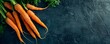 Fresh carrots with green tops on dark textured background