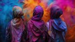 Trzy dziewczyny w hidżab stojące obok siebie w rzędzie sa obsypane intensywnymi barwami, tworząc kontrastowe i dynamiczne zdjęcie w dniu Holi