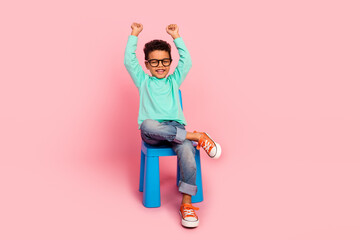 Poster - Full size photo of charming small boy sit chair raise fists specs dressed stylish cyan outfit isolated on pink color background