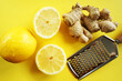 Whole and cut lemons next to ginger root and grater on yellow background